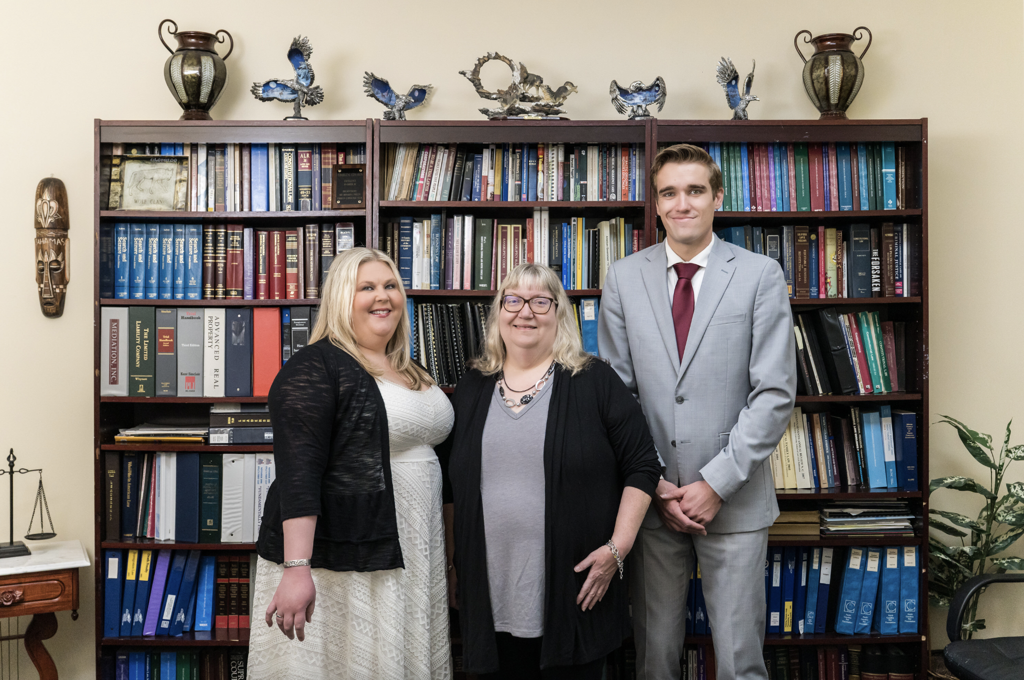 Team photo of divorce and custody experts April, Charlene, and Dylan standing in front of a bookcase in Lillington NC 
